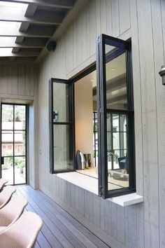 an open window on the side of a house next to chairs and windows with sliding glass doors