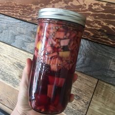 a hand holding a mason jar filled with pickles and other items on a wooden table