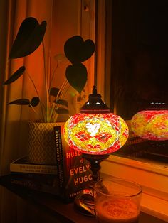 a lamp sitting on top of a wooden table next to a book and glass vase