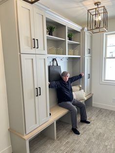 a man sitting on top of a wooden bench next to a white bookcase and cabinets