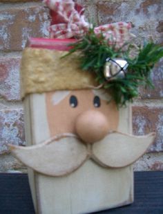 a wooden block with a santa clause on it's head and green plants in the top