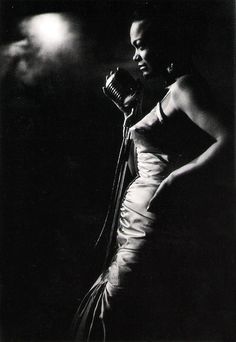 a black and white photo of a woman in a dress holding a microphone with her right hand