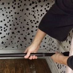 a person holding onto the handle of a black and white wallpapered room with wood floors