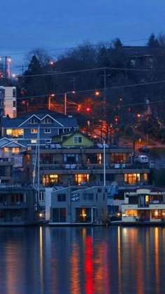 the city is lit up at night with lights reflecting in the water and houses on the other side