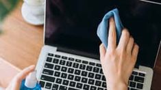 a woman is cleaning her laptop on the desk with a blue cloth in front of her