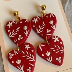 three red heart shaped earrings with white flowers on them