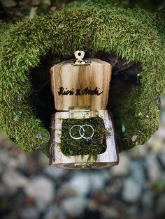 a wooden box with moss growing on it and two wedding rings in the bottom one