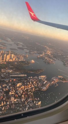 an airplane wing flying over a large body of water with buildings on both sides and a city in the distance