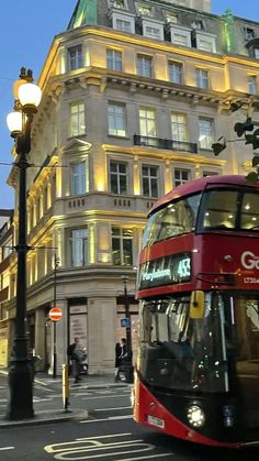 a red double decker bus driving down a street in front of a tall building at night