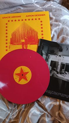 a red record sitting on top of a bed next to a book and an album