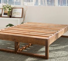 a wooden bed frame sitting on top of a carpeted floor next to a window