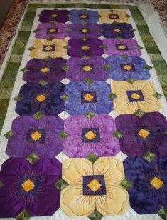 a quilted table runner with purple and yellow flowers on the top, along with green trim