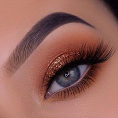 a woman's eye with gold glitters on her lashes and brown eyeshadp