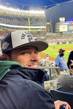 a man sitting in the stands at a baseball game wearing a hat and holding a cell phone