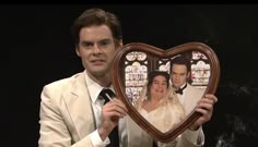 a man in a suit holding up a heart shaped frame with the image of two people on it