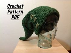 a green knitted hat sitting on top of a glass head mannequin's head