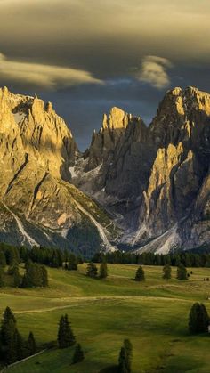 the mountains are covered in snow and green grass, with trees on either side of them