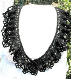 a black crocheted necklace is displayed on a mannequin neckline in front of some bushes