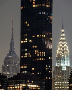 the empire building is lit up at night in new york city, with other skyscrapers behind it