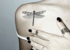 a woman's back with dragonfly tattoos on her left shoulder and fingernails