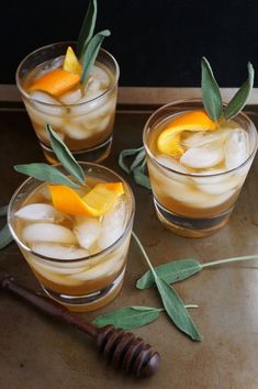 three glasses filled with drinks and garnished with orange peels, leaves and honey