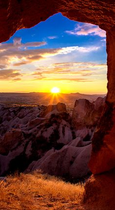 the sun is setting through an opening in a rock formation