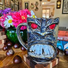 a mug with a face on it sitting next to some flowers and other items in the background