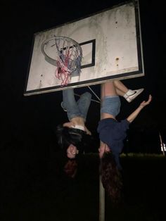 two girls are hanging upside down on a basketball court while one girl is holding onto the backboard