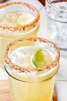 two margaritas sitting on top of a wooden cutting board