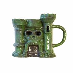 a green ceramic mug with a skull on it's face and two hands in the shape of a castle