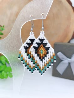 a pair of beaded earrings on top of a wooden table next to a present box