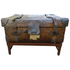 an old trunk sitting on top of a wooden stand with leather straps and latches