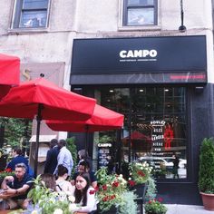 people sitting at tables in front of a store with red umbrellas and flowers outside