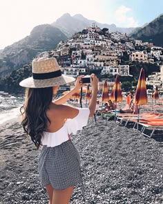 a woman standing on top of a beach next to an umbrella covered hill with buildings in the background