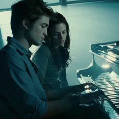 a man and woman standing next to each other in front of a piano with their hands on the keys