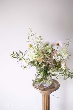 a vase filled with lots of flowers sitting on top of a wooden table next to a white wall