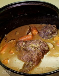 a pot filled with meat and carrots on top of a stove