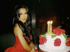 a woman sitting in front of a cake with candles on it and roses around the edges