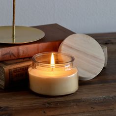 a lit candle sitting on top of a wooden table next to books and a plate