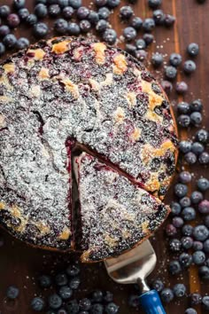 a blueberry pie on a wooden table with fresh blueberries around it and a slice taken out