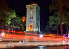 a tall clock tower sitting on the side of a road next to trees at night