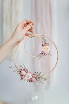 a hand holding a hoop with flowers hanging from it's side and another hand holding the hoop