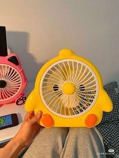 a person holding a yellow and pink fan on top of a desk next to other items