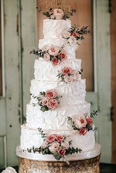 a white wedding cake with pink flowers and greenery on top sits on a gold platter