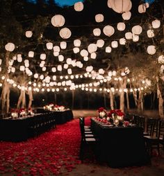 an outdoor dinner setup with paper lanterns and red rose petals on the ground at night