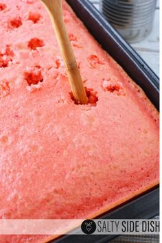 a wooden spatula is being used to dip into a red cake in a pan