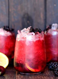 two glasses filled with blackberry lemonade on top of a wooden table next to fruit