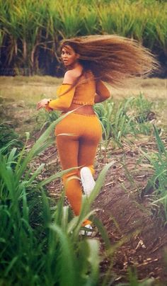 a woman with long hair walking through tall grass