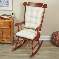 a wooden rocking chair with white cushions in a room next to a bookcase and small table