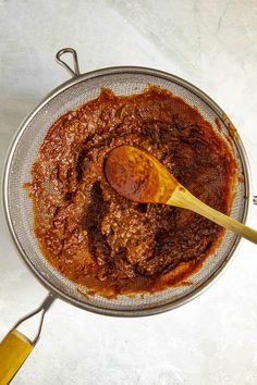 a wooden spoon in a metal bowl filled with red sauce on top of a white counter